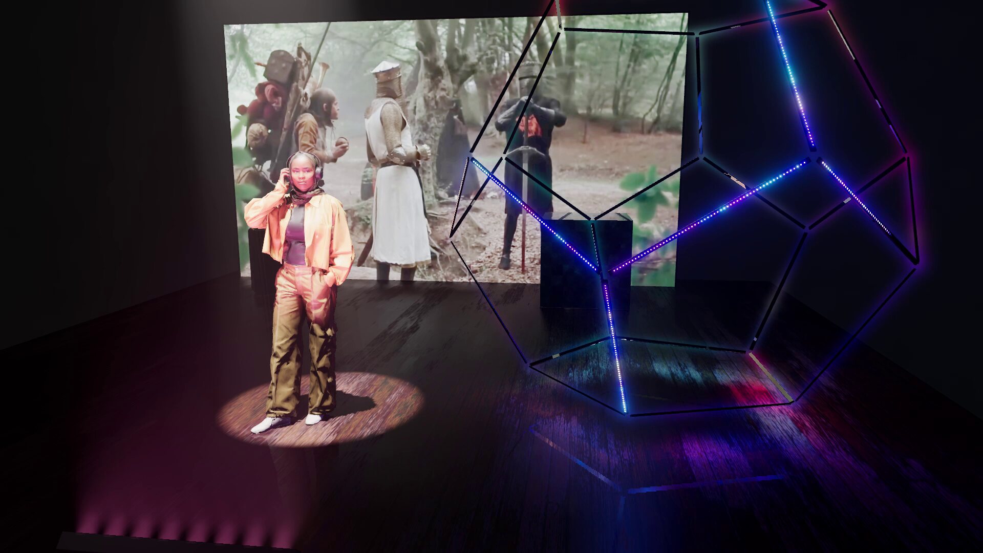 A video playing on a screen at the back of a stage, a large dodecahedron of LED bars glowing blue and magenta on a reflective wooden floor, and a 3D figure standing in a spotlight